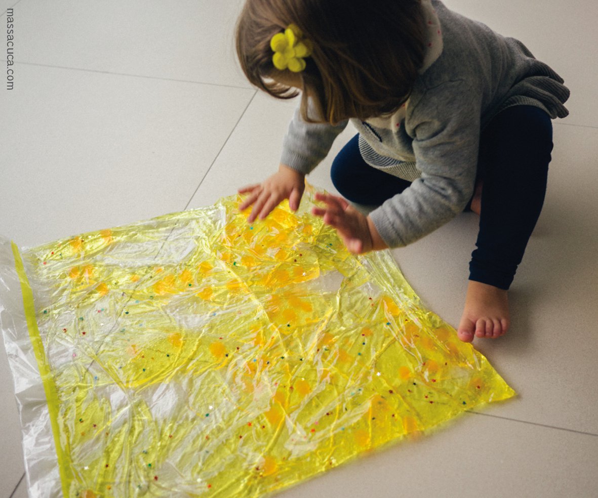 Saco sensorial: foto de uma menina que brinca no chão e mexe em um saco transparente e amarelo.