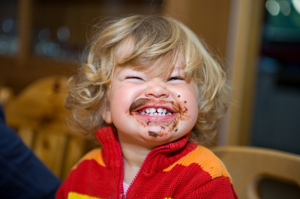 Menino loiro sorrindo para a câmera com a boca suja de comida