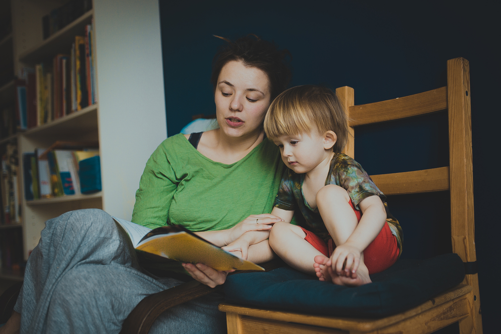 Mulher e criança lendo um livro infantil sentados em uma cadeira de madeira.