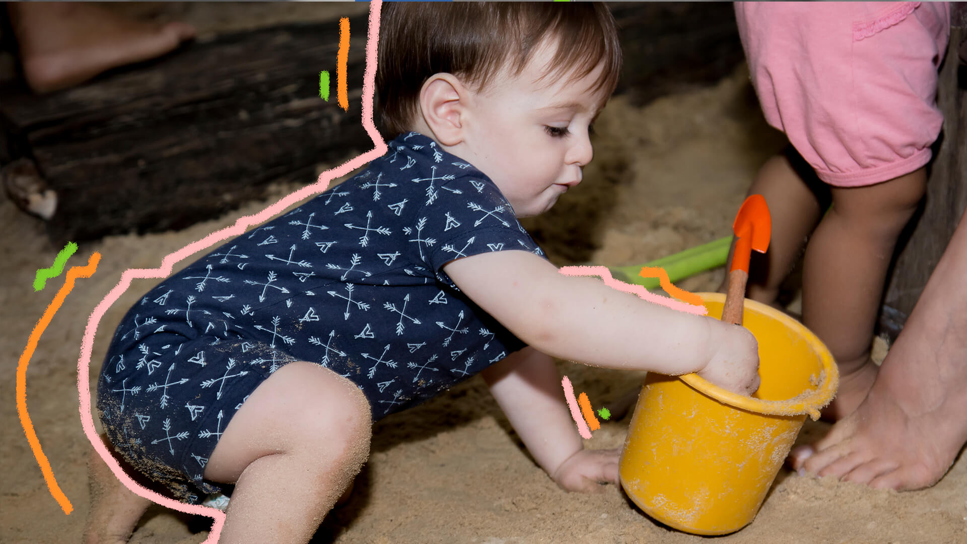 Bebê engatinhando brincando na areia com um baldinho.