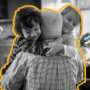 Foto em preto e branco mostra um homem de costas num abraço com duas crianças