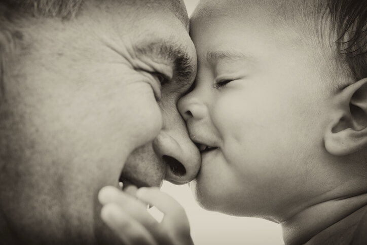 Foto de um bebê beijando o nariz de um homem. Ambos estão de olhos fechados.