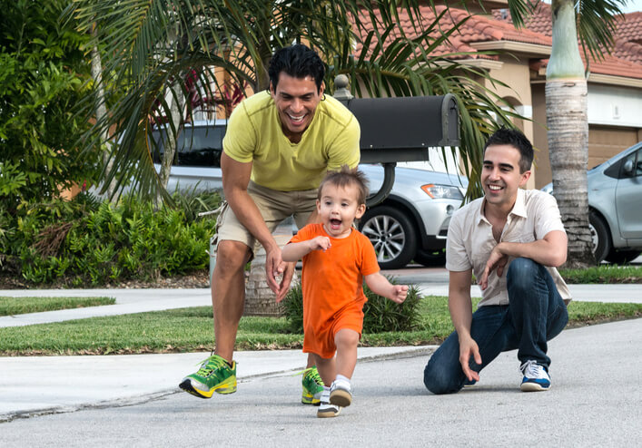 Foto de dois homens que brincam com uma criança na rua. A dupla observa o menino correr.