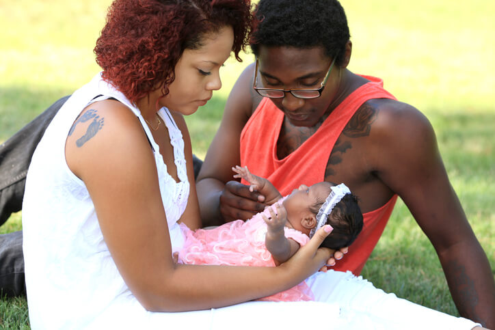 Foto de um casal que olha para seu bebê recém-nascido em um gramado