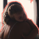 Em um abraço menino deita no ombro da mãe que o abraça, enquanto ele repousa o rosto em seu ombro.