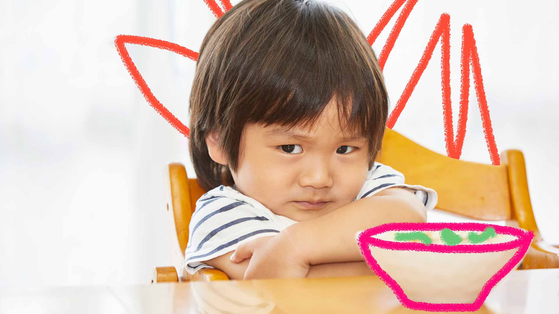Um menino sentado em uma cadeira olha para a câmera com uma expressão de que não quer comer. Na sua frente, um prato de comida.