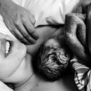 Foto em preto e branco mostra mãe e bebê deitados. O recém-nascido está no colo da mãe e ela sorri.