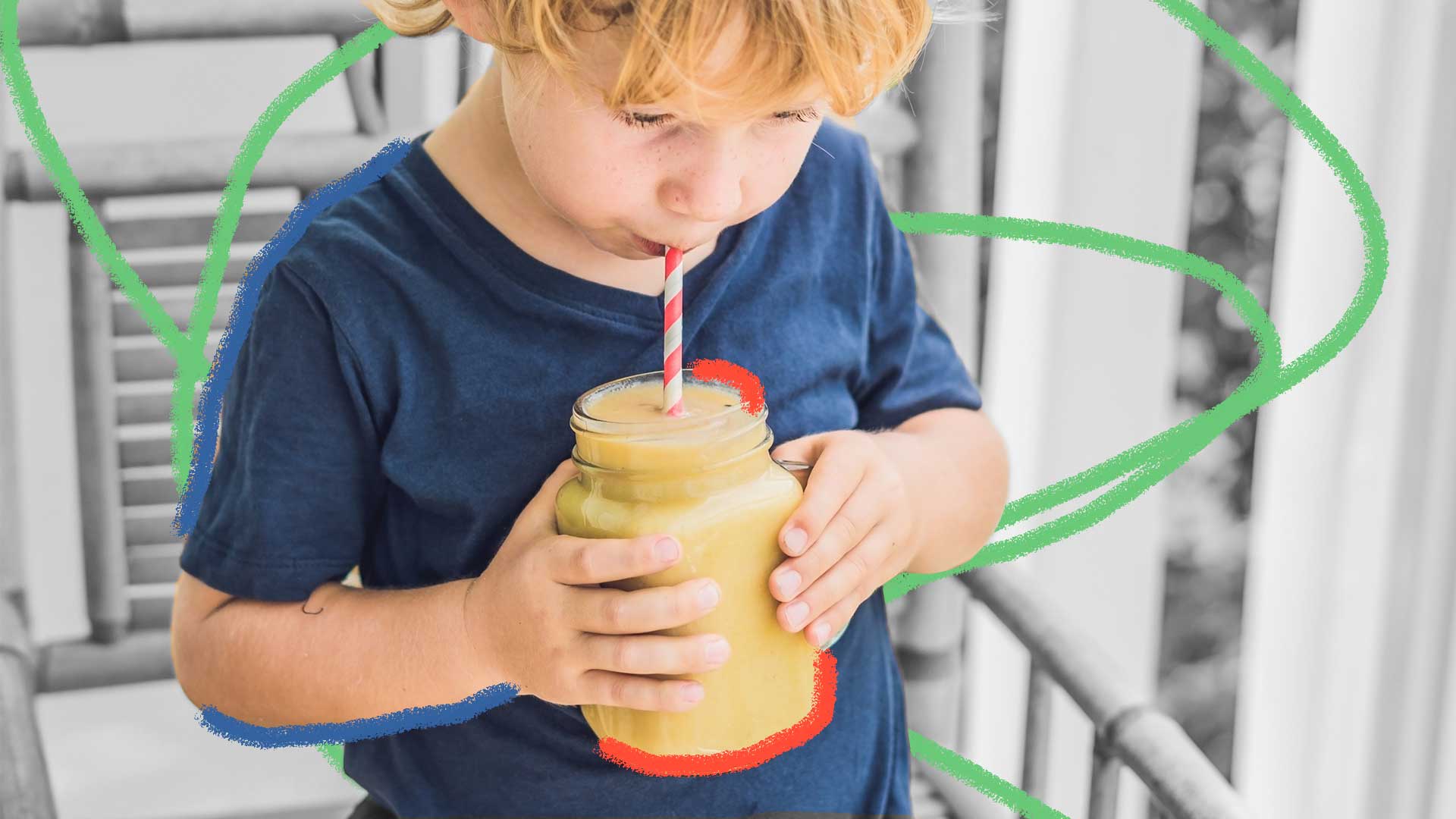Um menino de camiseta azul segura um pote com um suco amarelo, enquanto bebe por um canudo