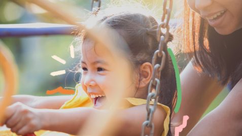 Uma menina asiática brinca num parquinho. Atrás dela, aparece partes de uma mulher adulta