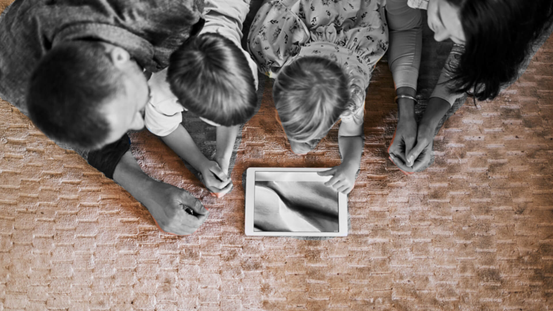 Um homem, um mulher e uma criança olham para um tablet apoiados com os cotovelos no chão