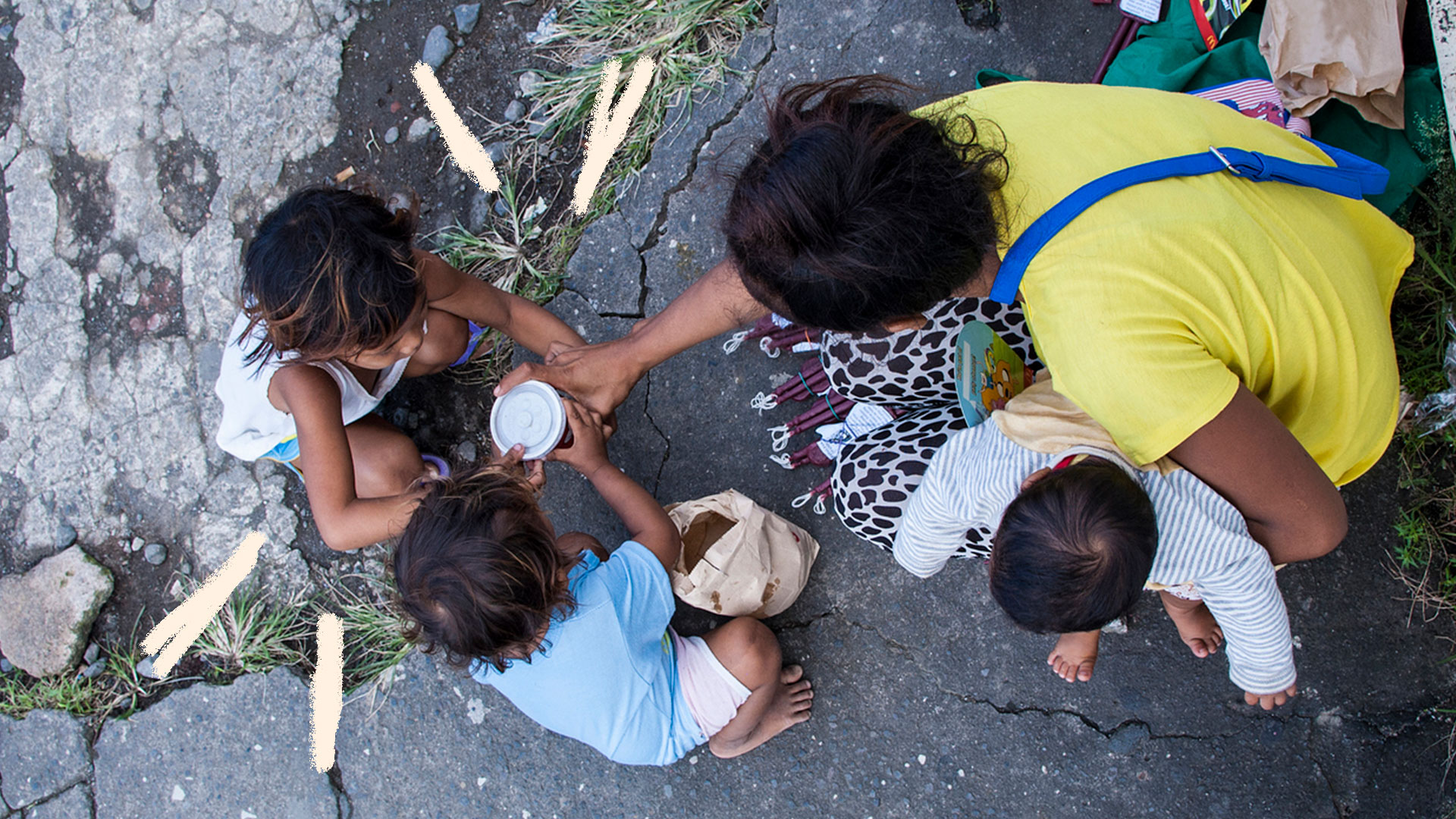 Mulher adulta e três crianças em situação de rua, sentados na calçada de cabeça abaixada.