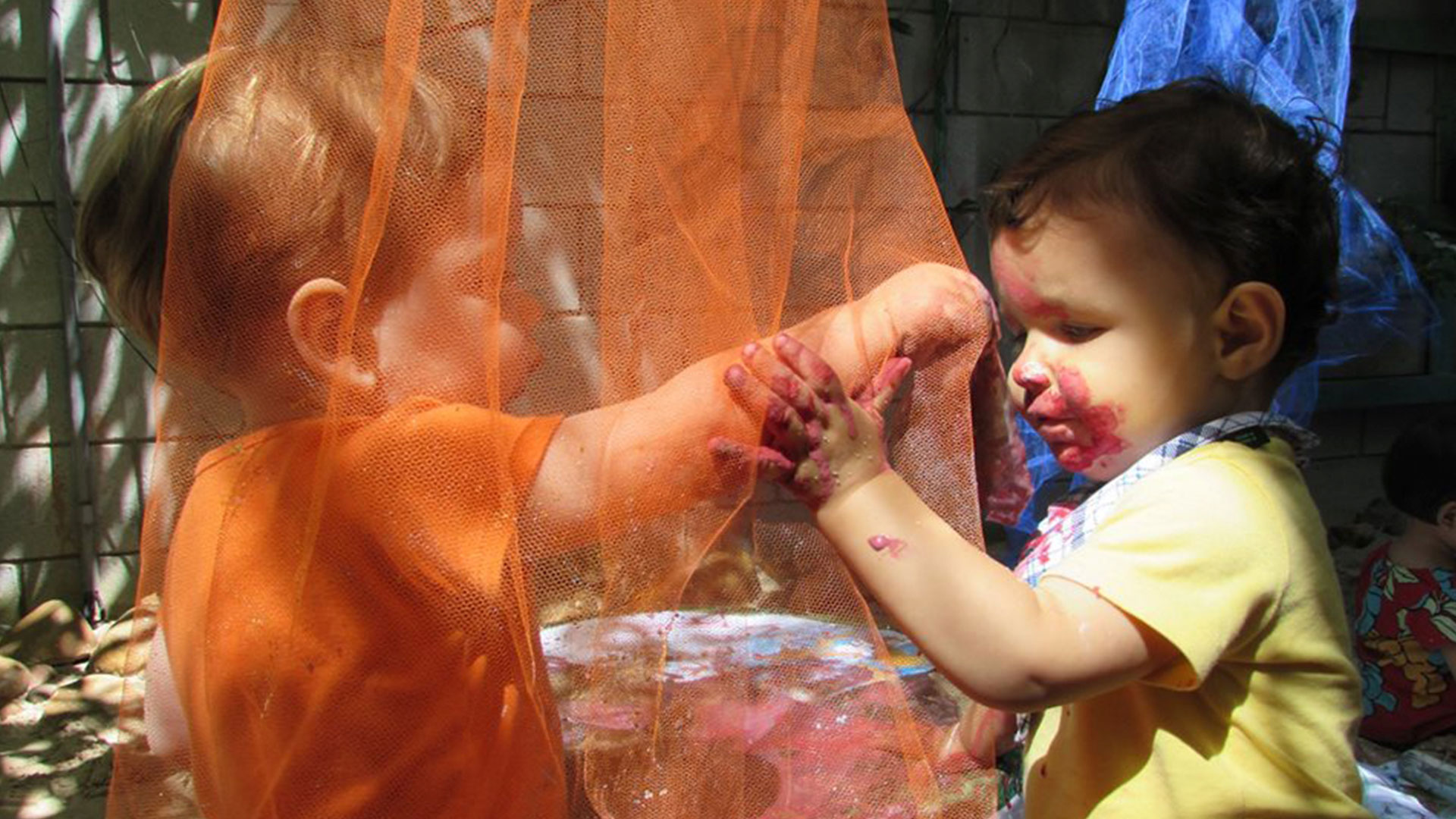 Dois bebês brincam de explorar texturas de tule cor de laranja