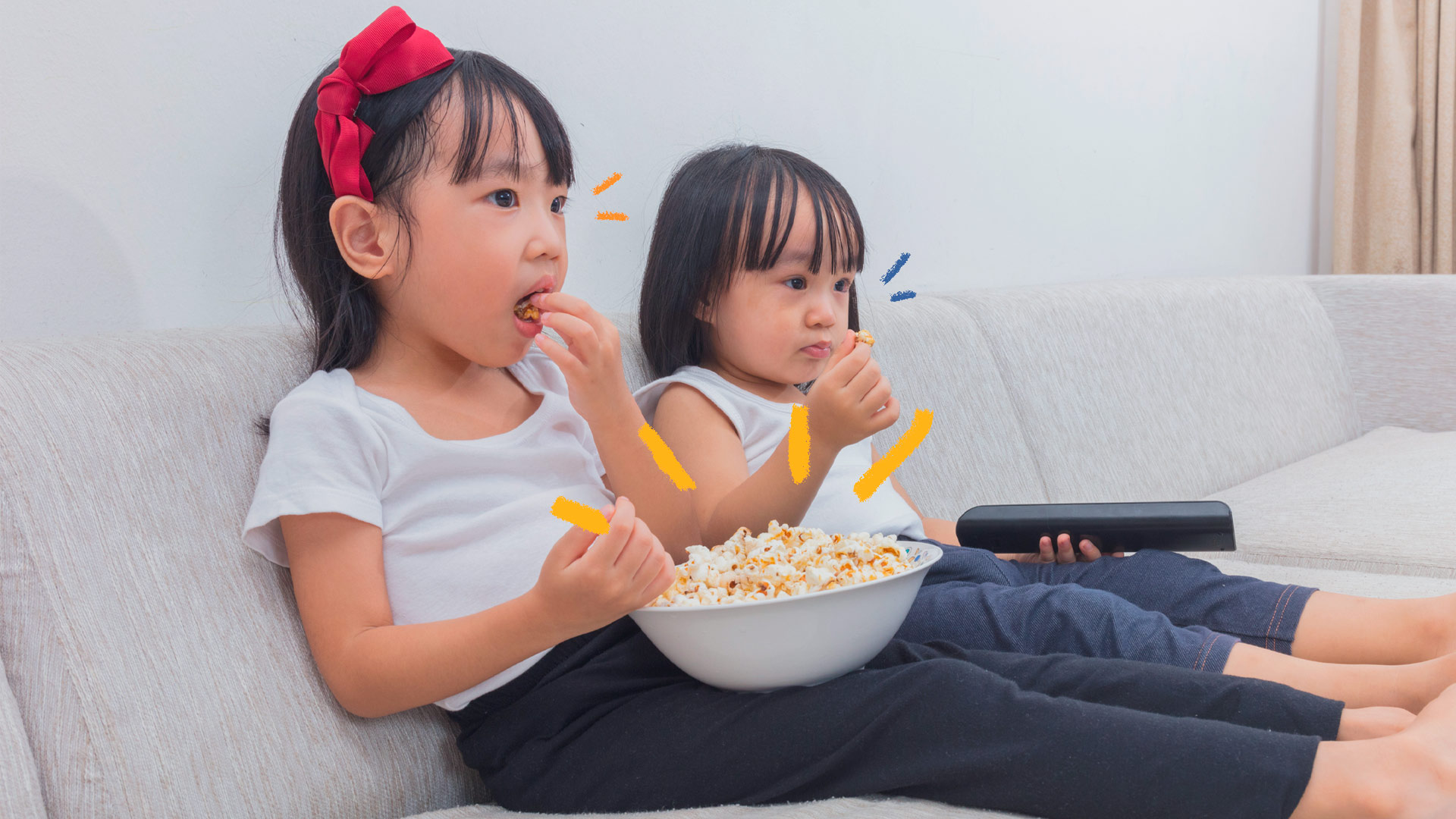 Filmes sobre autismo foto de duas meninas sentadas no sofá assistindo a um filme. A maior delas segura uma bacia de pipoca e a outra segura o controle remoto