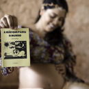 A poeta Mariane Bigio grávida segurando o cordel "A mãe que pariu o mundo" com uma das mãos, e com a outra alisando a barriga.