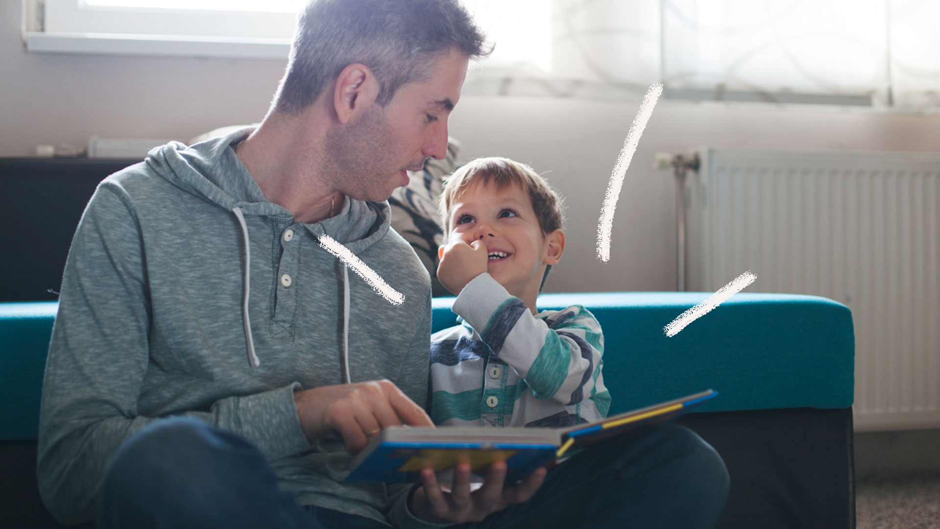 Homem adulto lê com criança sentado no chão da sala, com livro infantil no colo.