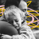 Homem adulto abraça criança chorando em foto preto e branca com grafismos amarelos e cor-de-rosa