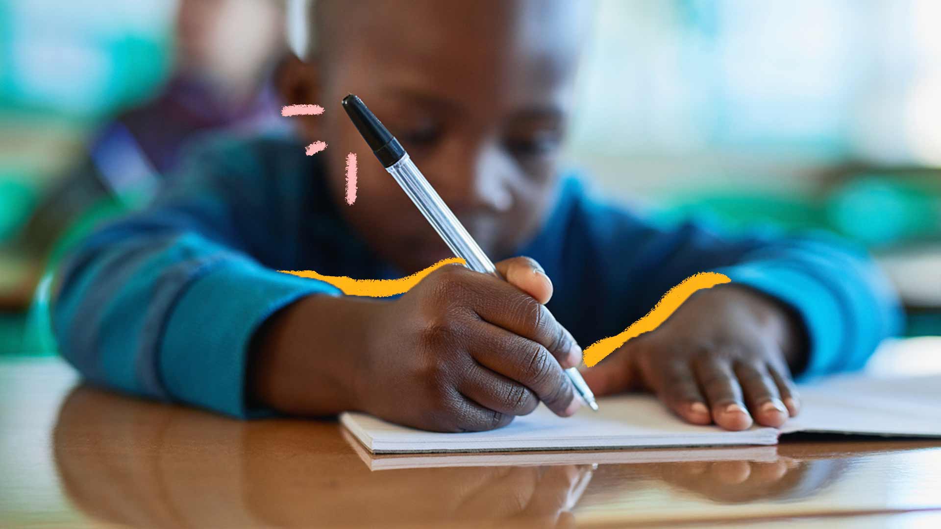 Uma imagem de um menino negro sentado e escrevendo. A foto mostra seu rosto desfocado e sua mão em primeiro plano focada