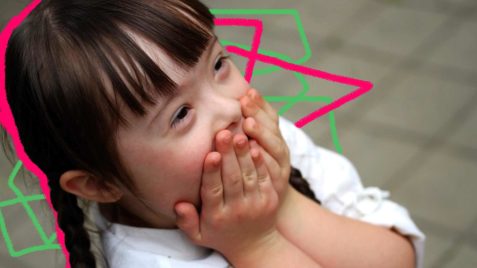 Foto de uma criança com síndrome de Down com as duas mãos tampando a boca