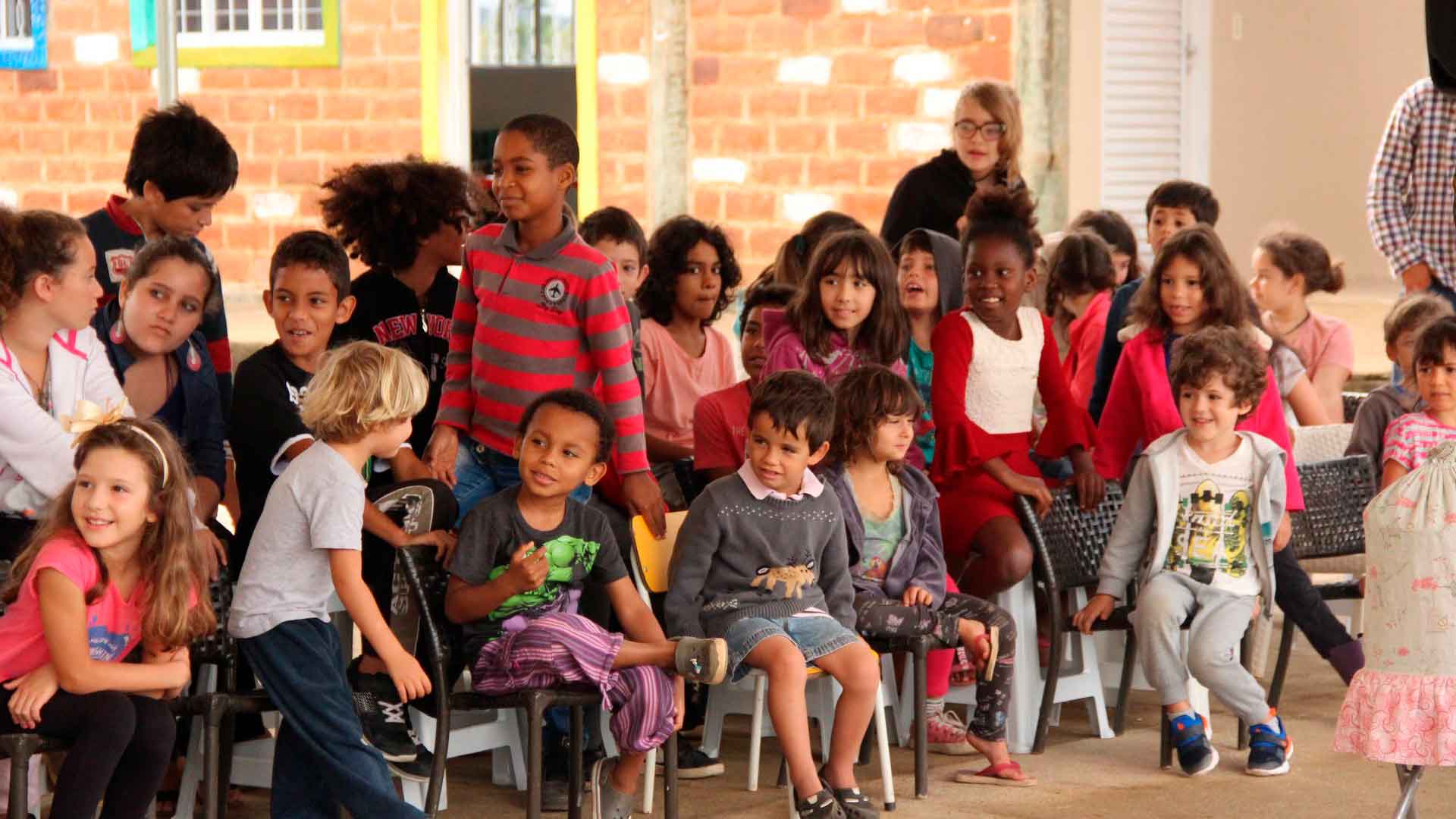 Foto de um grupo de mais de 15 crianças, algumas sentadas e outras em pé, alinhadas em fileiras horizontais