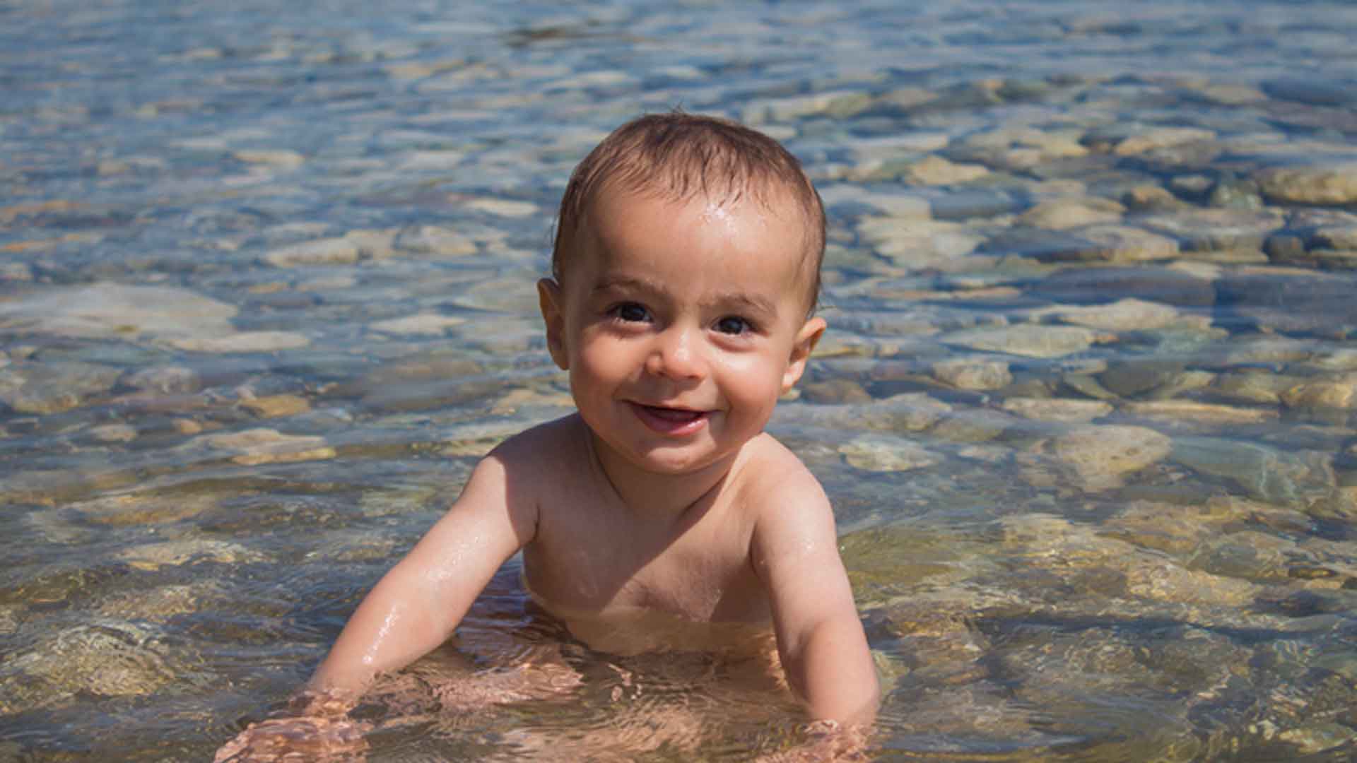 Foto de um bebê sorrindo sentado na água