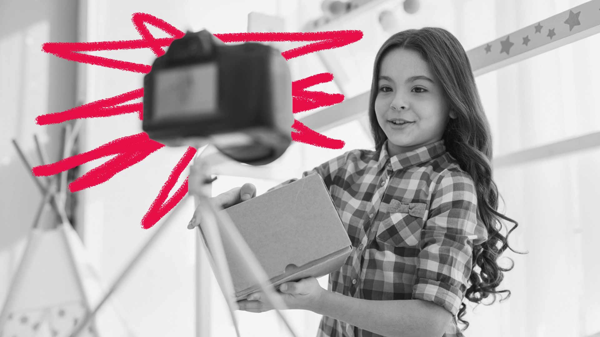 Foto em preto e branco de uma menina com um notebook na mão e uma câmera no tripé. Ela está se filmando.