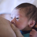 Foto de um peito amamentando um bebê. O bebê está com olhar fixo enquanto está mamando