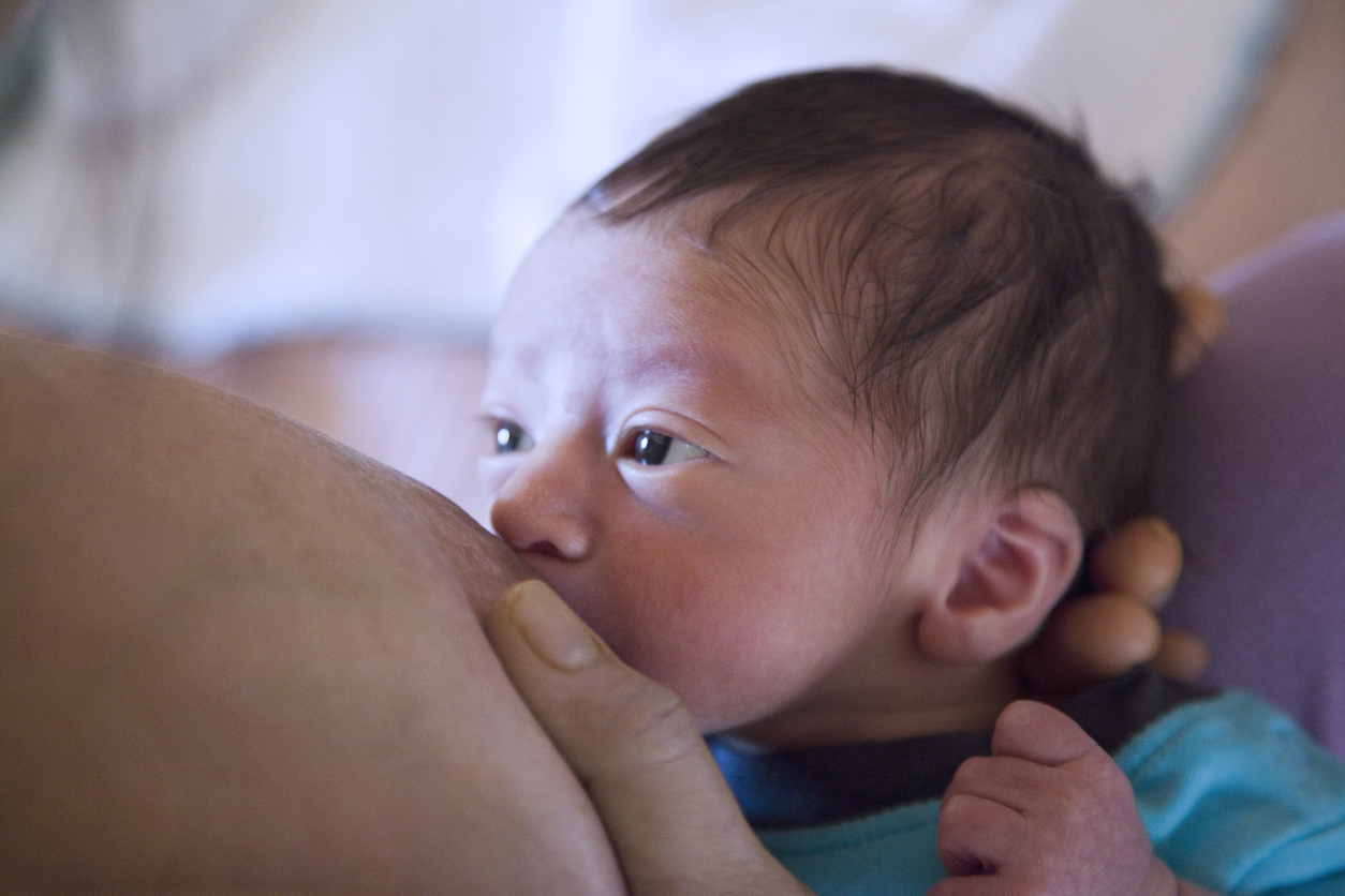 Bebê rejeita o peito: foto de um peito amamentando um bebê. O bebê está com olhar fixo enquanto está mamando.