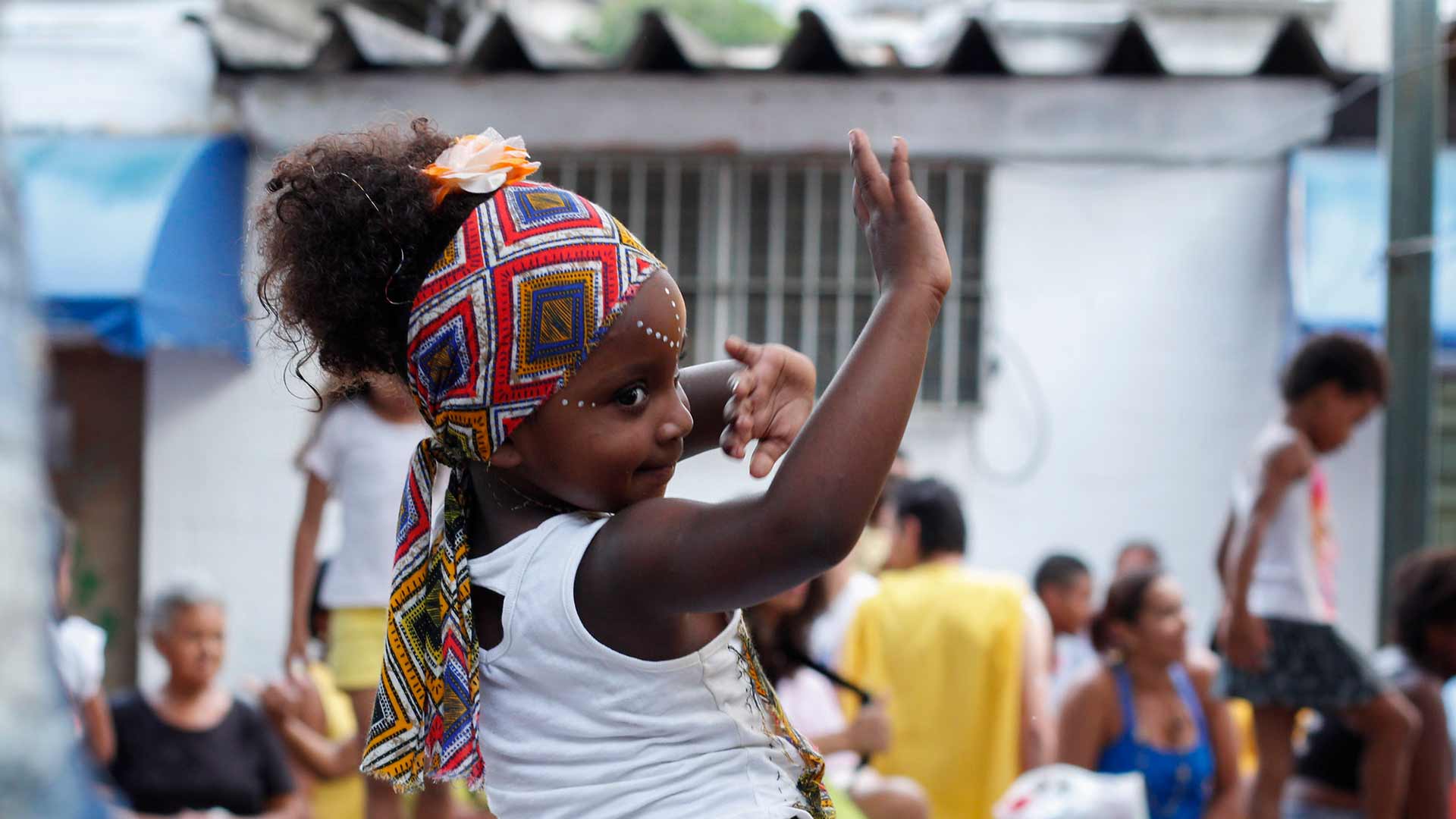 Foto de criança negra com um lenço na cabeça, dançando e fazendo movimentos com as mãos