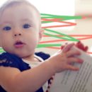 Foto de um bebê com as duas mãos segurando um livro, ele está olhando para o lado