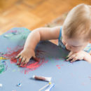 Imagem de um bebe com a mão de tinta passando em cima da mesa