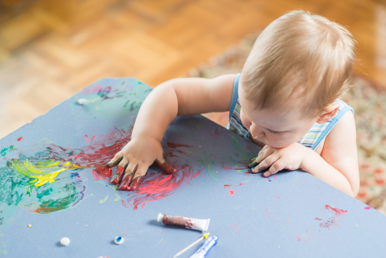 Imagem de um bebe com a mão de tinta passando em cima da mesa