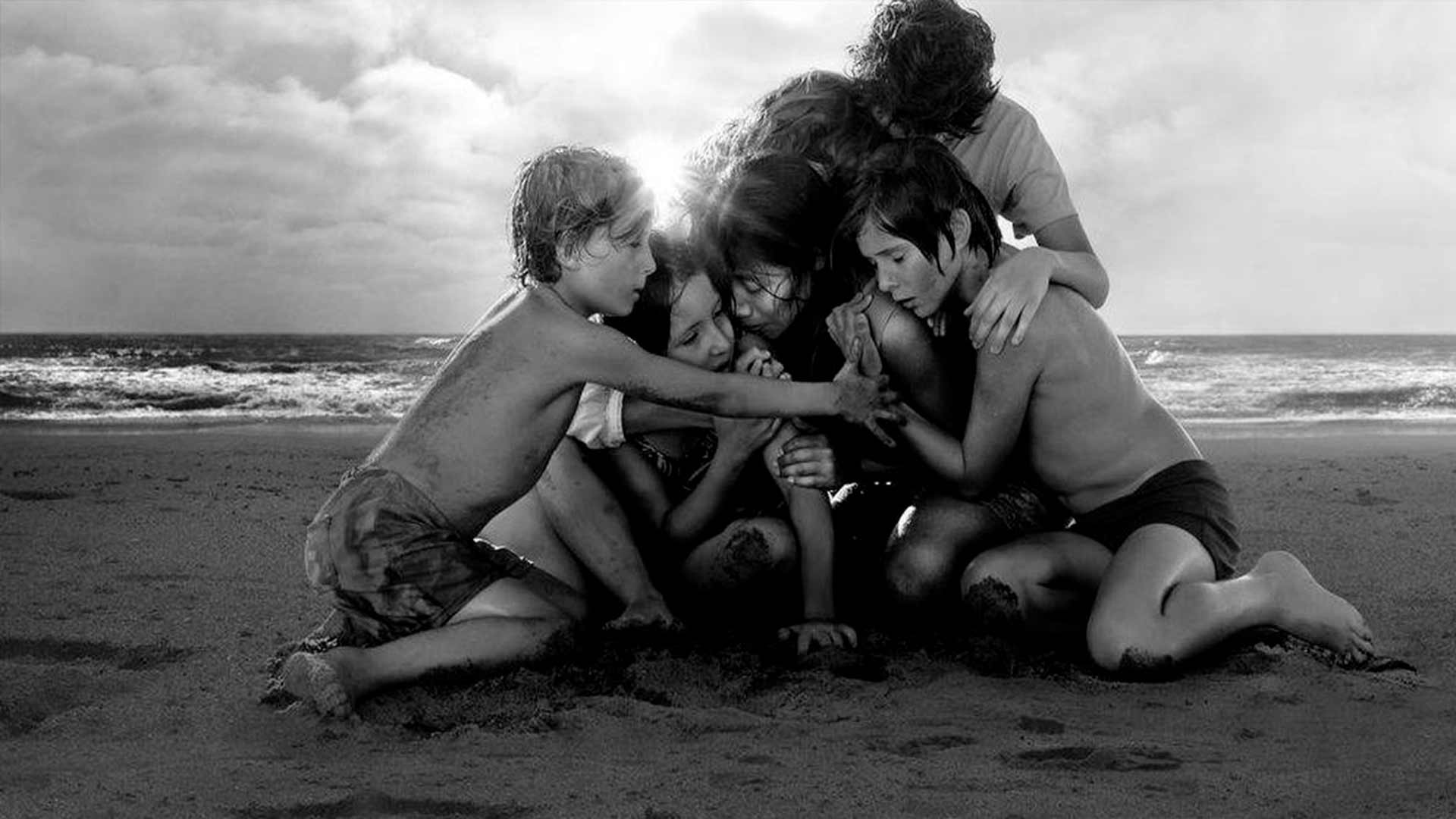  Imagem preto e branco, de crianças sentadas em uma areia se abraçando com os olhos fechados