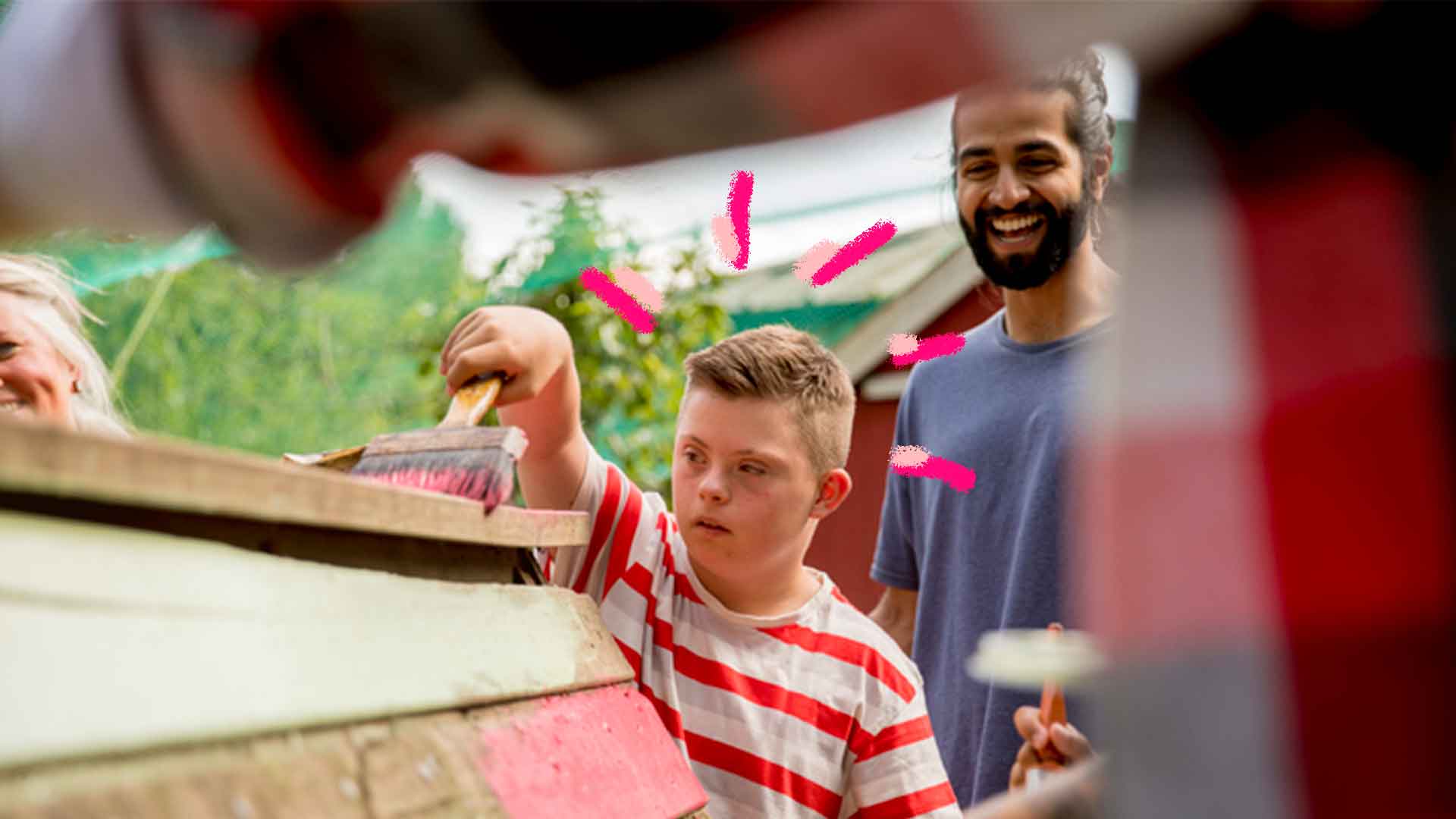 Imagem de um menino com pincel pintando uma parede, atrás dele há um homem que olha para o menino e sorri.
