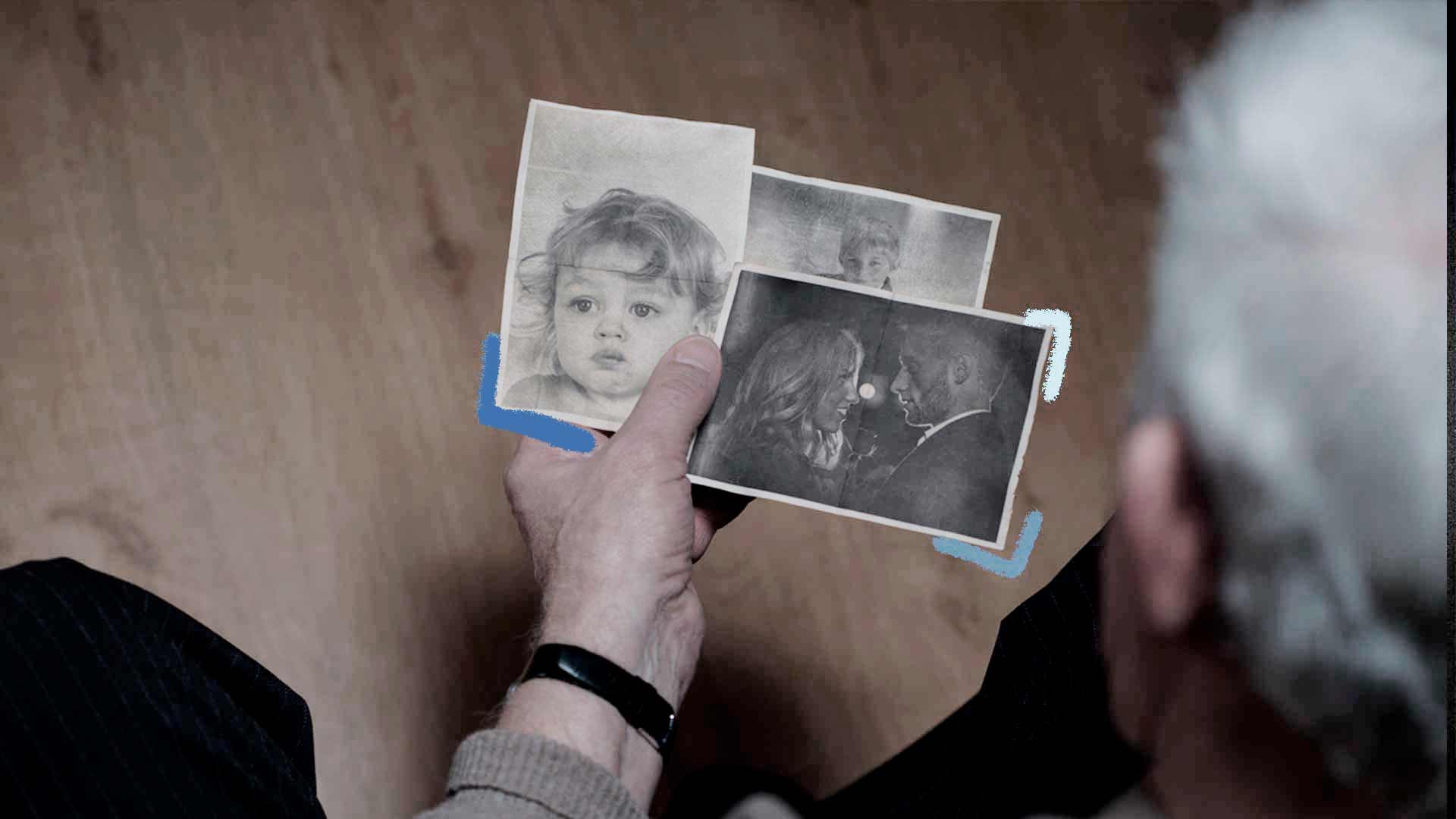 Foto de uma mão, segurando três retratos em preto e branco, uma foto de um bêbe, outro de um casal, e outra de uma criança, cujo as três fotos estão juntas em suas mãos