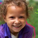 Foto de uma criança sorrindo em primeiro plano, atrás uma imagem fosca com o fundo verde