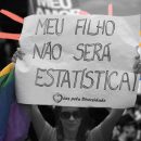 Coletivos de mães: Foto em preto e branco de uma mulher com um cartaz levantado escrito: "Meu filho não será estatística", e com a bandeira LGBT em suas mãos