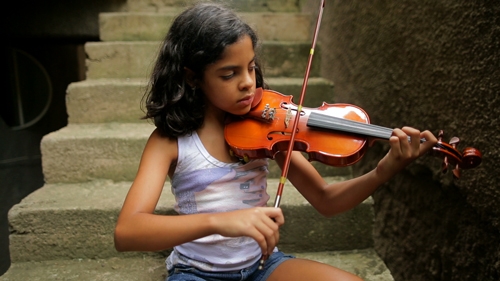 Foto de uma criança sentada em uma escada, tocando violino com os olhos fechados
