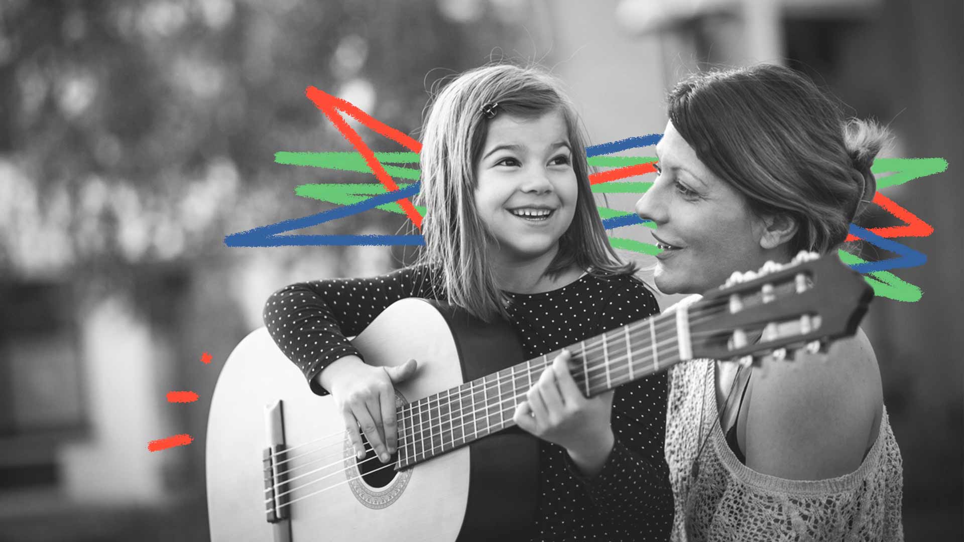 Foto preto e branco de uma mãe e uma menina. A menina está tocando violão, e as duas estão cantando felizes