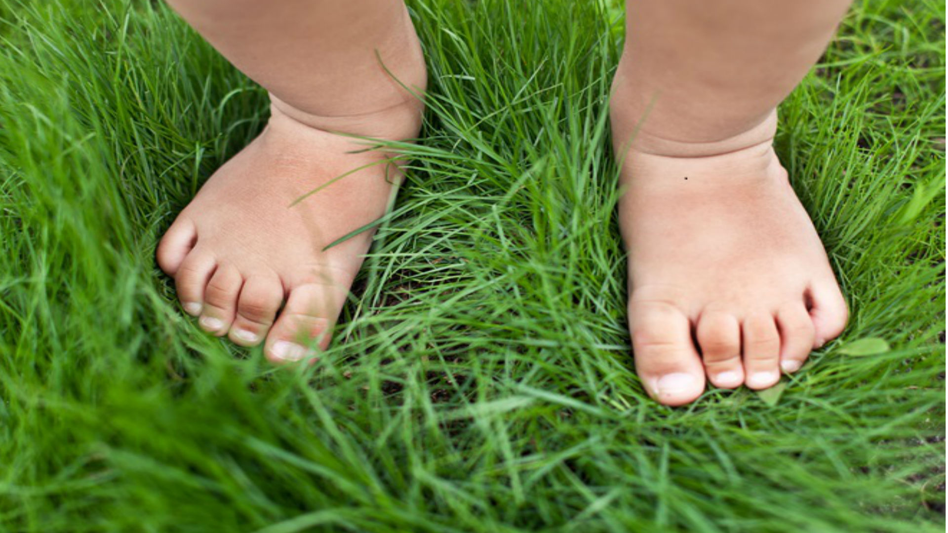Foto de uma grama e os pés de um bebê pisando em cima