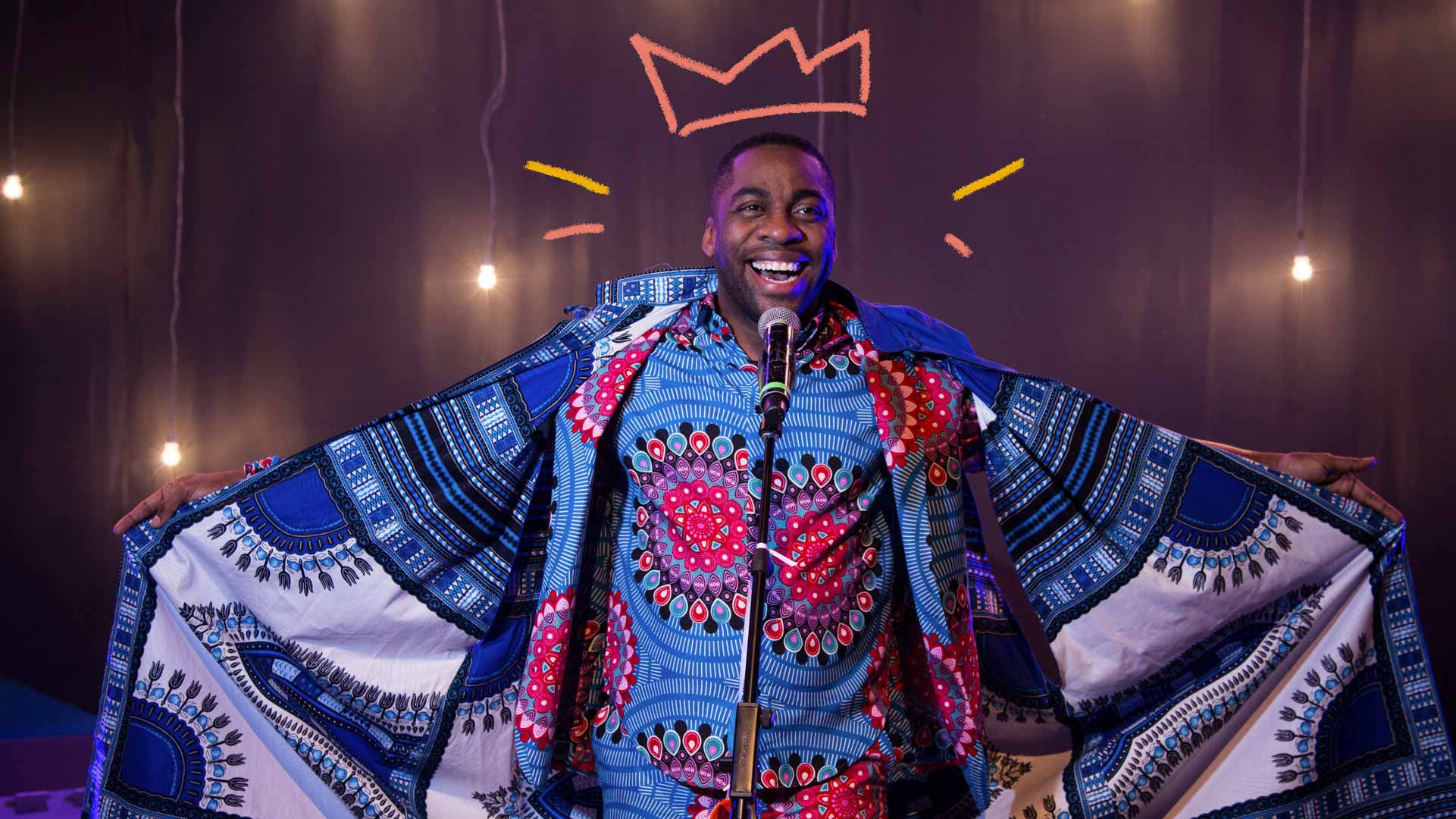 Imagem de Lázaro Ramos: ator, apresentador e diretor. Está com uma capa de rei, sorrindo e falando ao microfone.