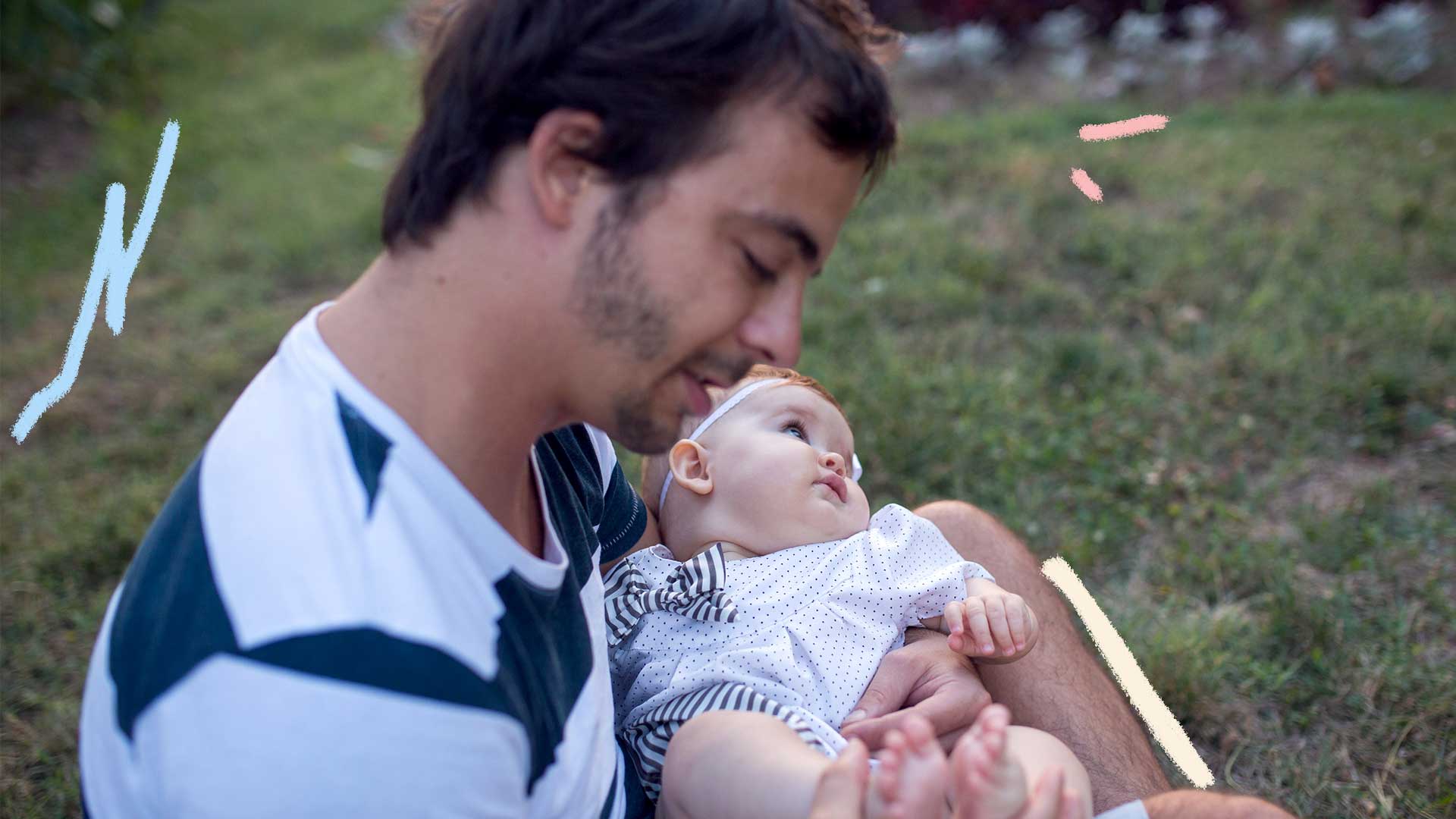 Imagem de um homem segurando um bebê em seu colo. Eles estão em um jardim