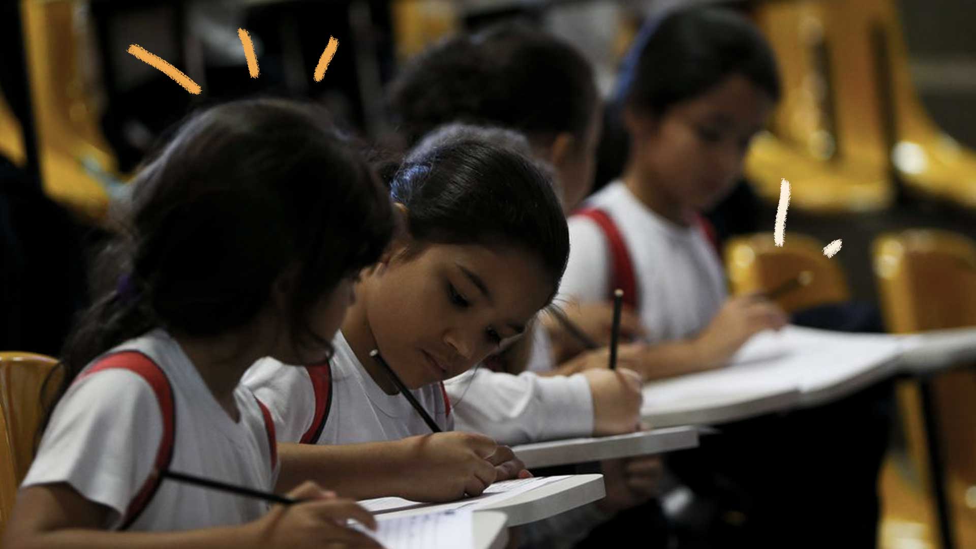 Foto de crianças sentadas em sala de aula escrevendo com seus lápis em seus cadernos