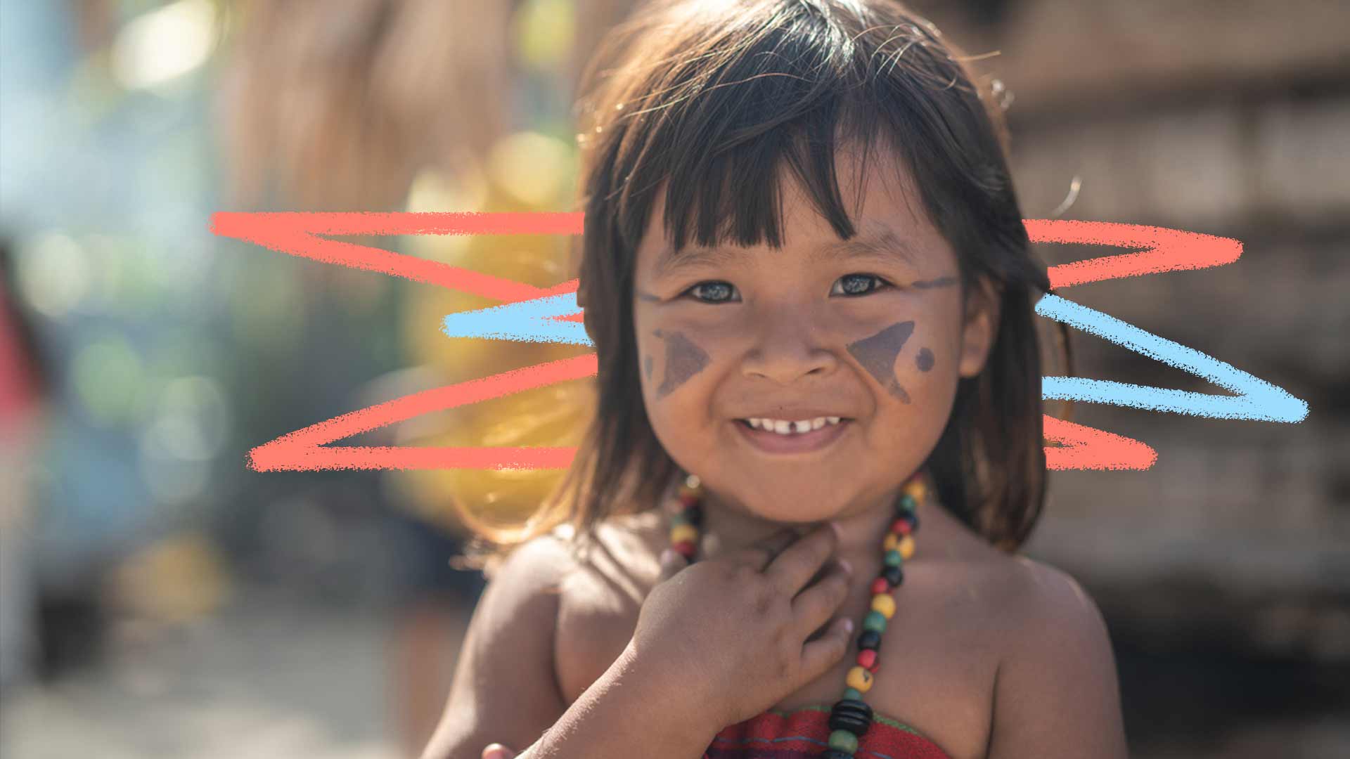 Foto de uma criança indígena sorrindo com um cocar no pescoço e seu rosto pintado.