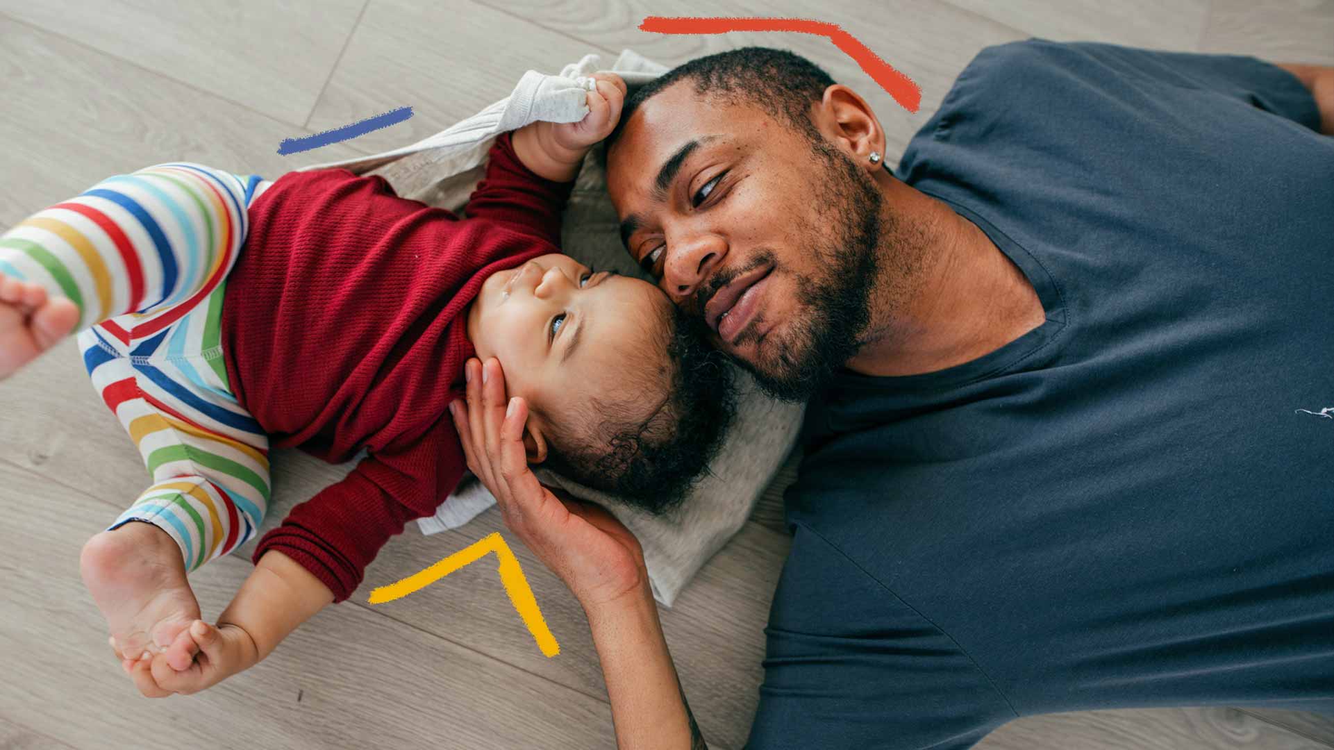 Imagem de um homem negro com um bebê deitado no chão. O homem faz carinho no bebê.