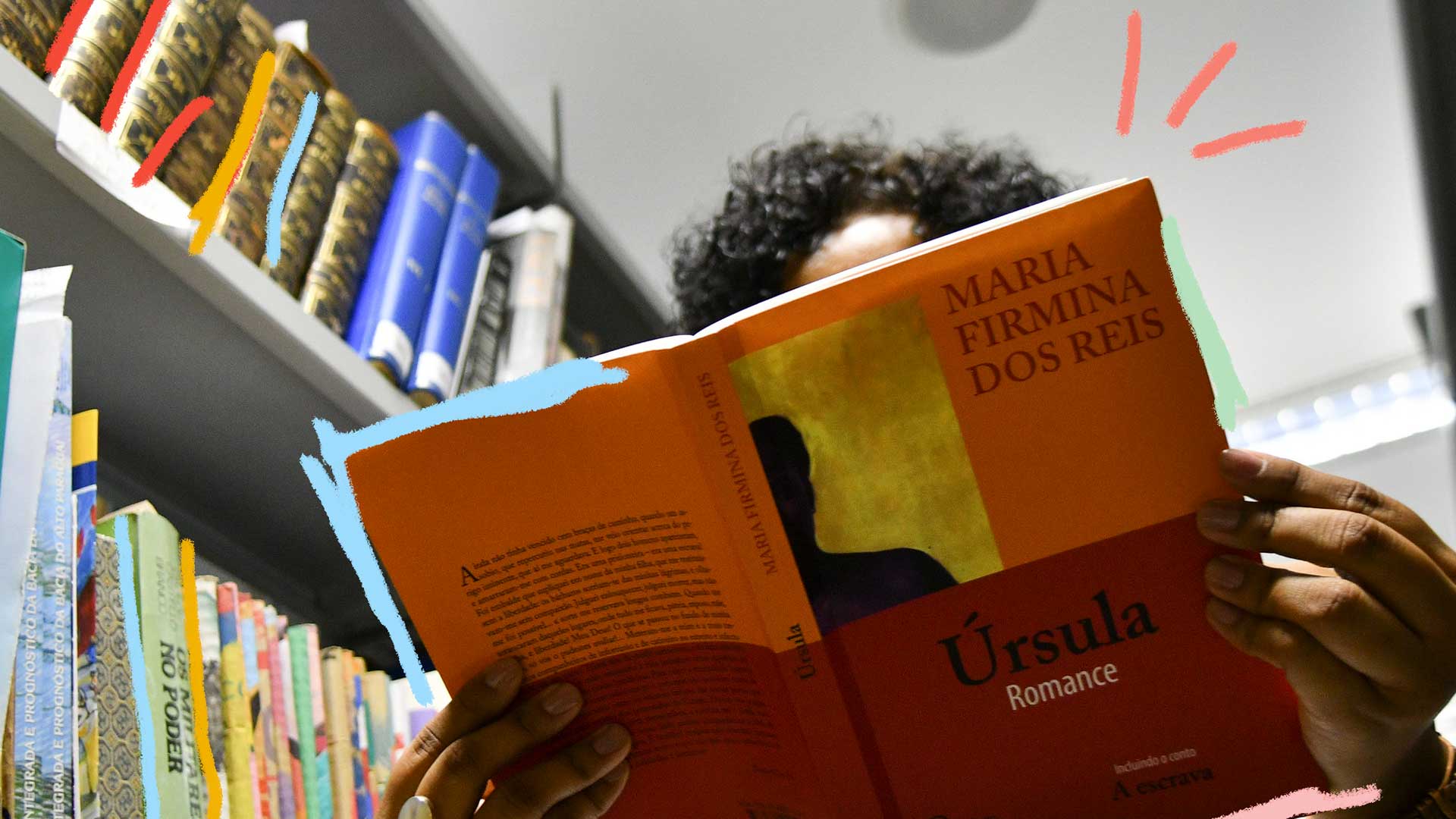 Foto de uma mulher lendo o livro de “Maria Firmina dos Reis”, Úrsula. Na imagem aparece uma biblioteca e a mão de uma mulher segurando o livro.