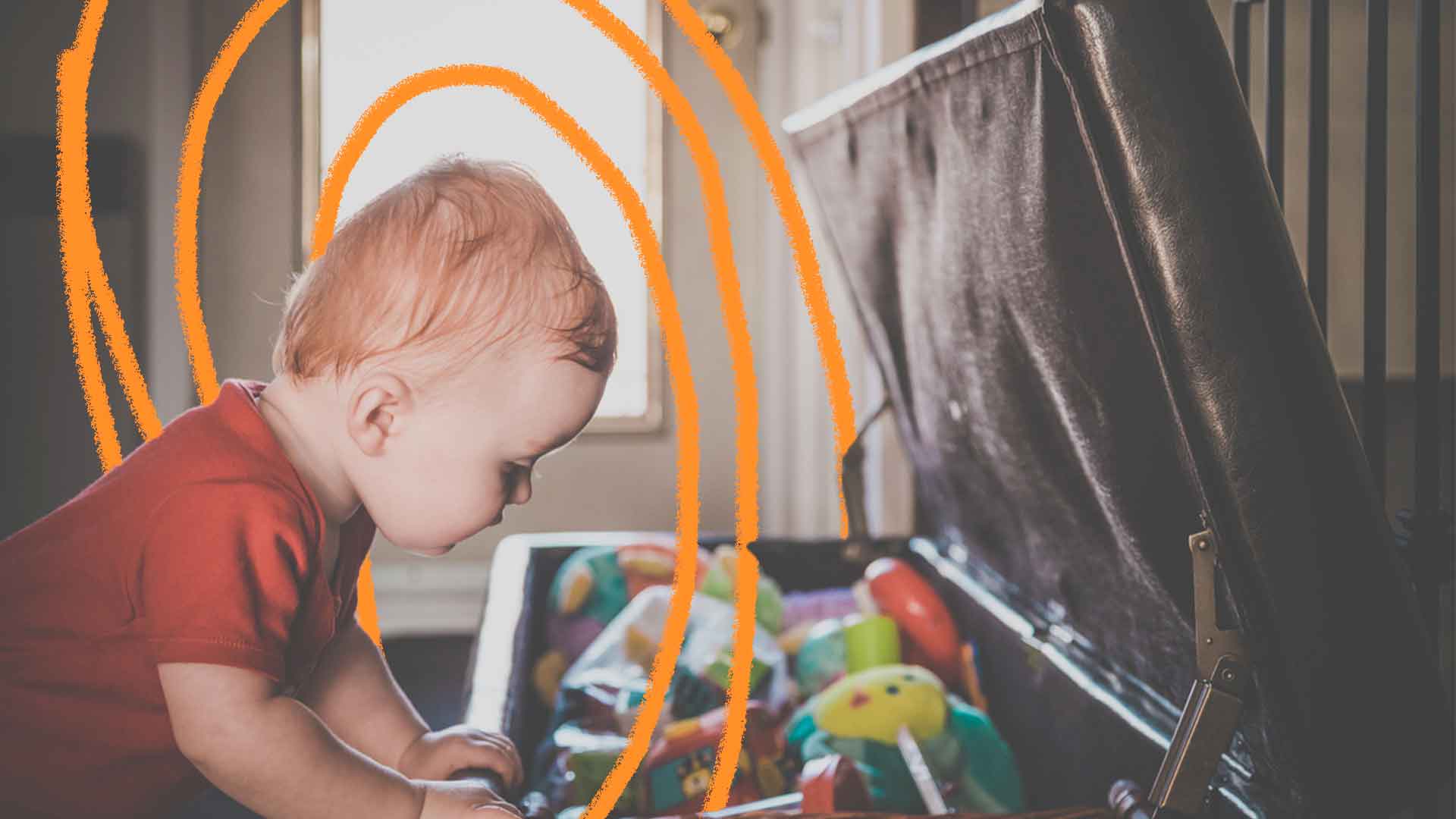 Imagem de um bebê debruçado se apoiando em um baú cheio de brinquedos.