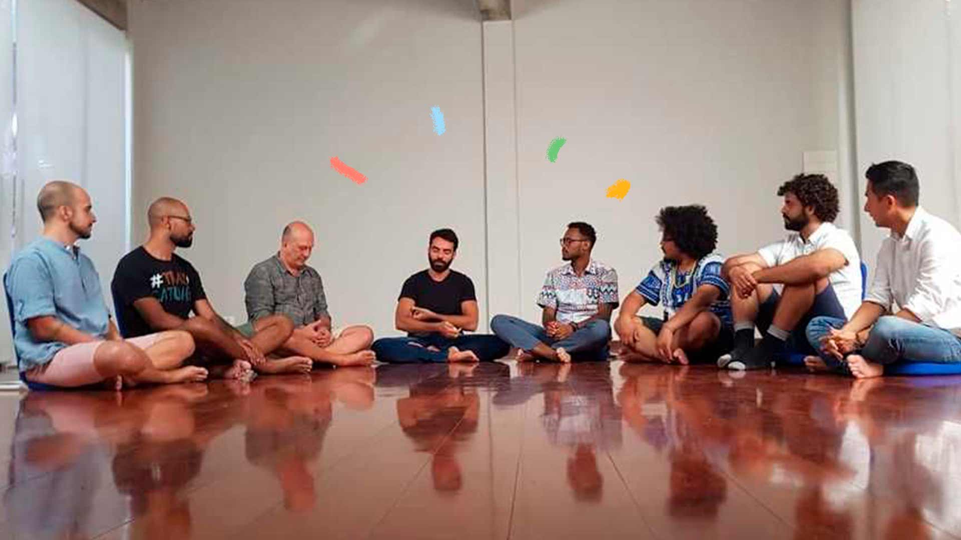 Imagem de oito homens sentados enfileirados no chão, conversando.