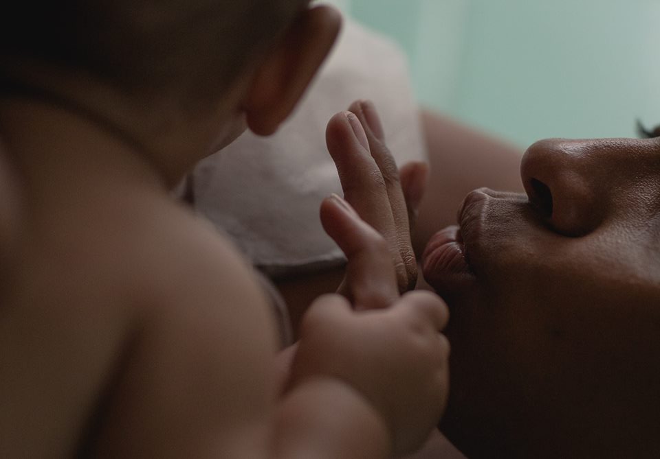 Foto de uma boca fazendo bico e um bebê está segurando uma das mãos