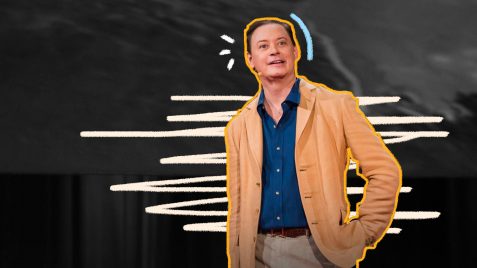 Andrew Solomon, um homem branco de cabelos levemente ruivos, vestindo uma calça bege, camisa azul marinho e jaqueta tarja