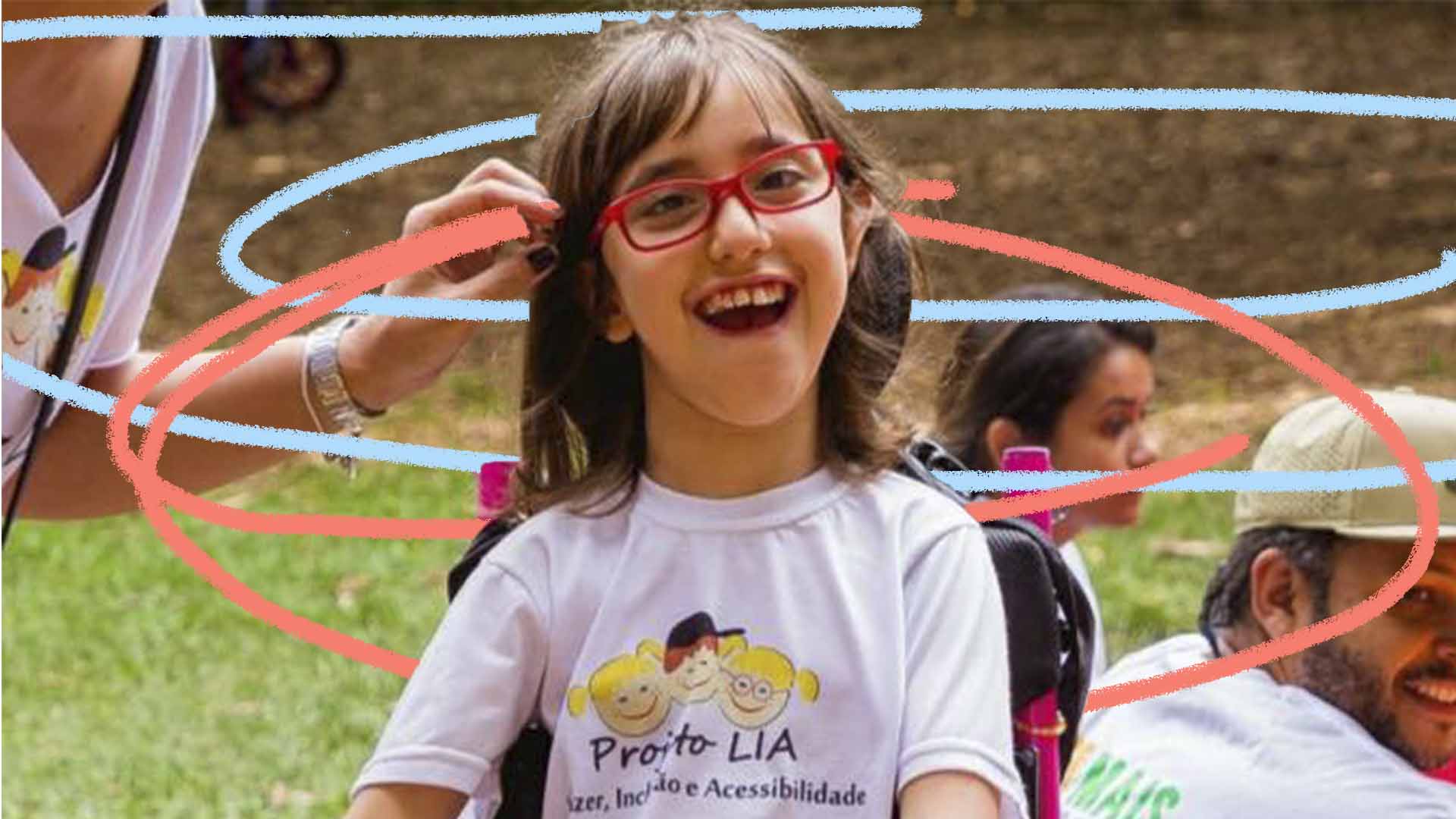 Imagem de uma criança com paralisia cerebral. Ela está em uma cadeira de rodas sorrindo com uma camiseta do projeto Lia